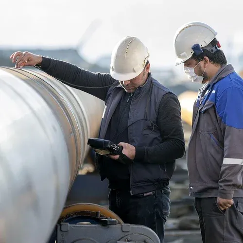 Dos técnicos con casco inspeccionan una tubería industrial con un equipo portátil